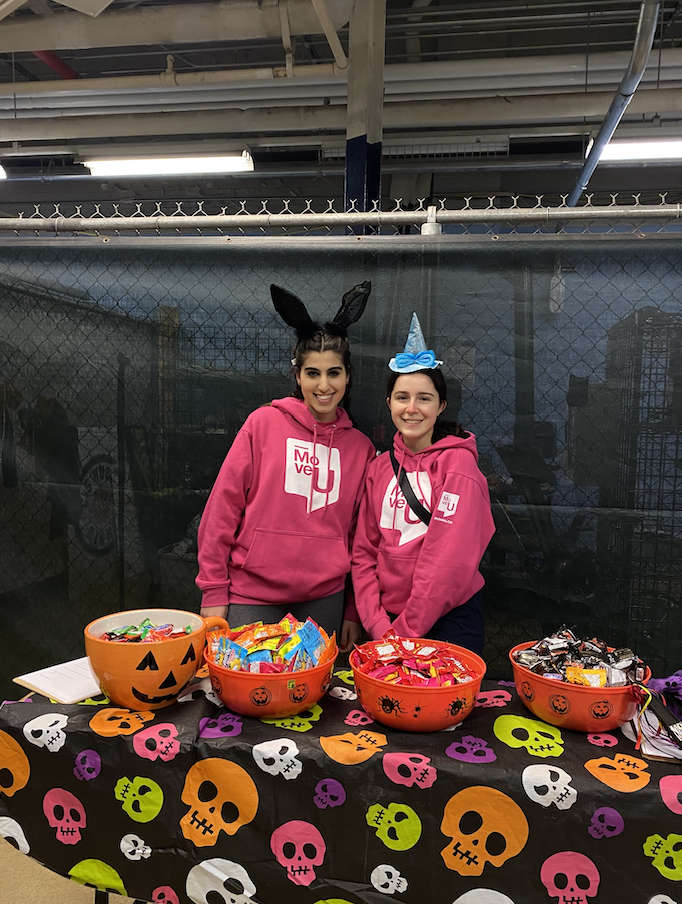 Two members of the MoveU team behind a table of Halloween candy.