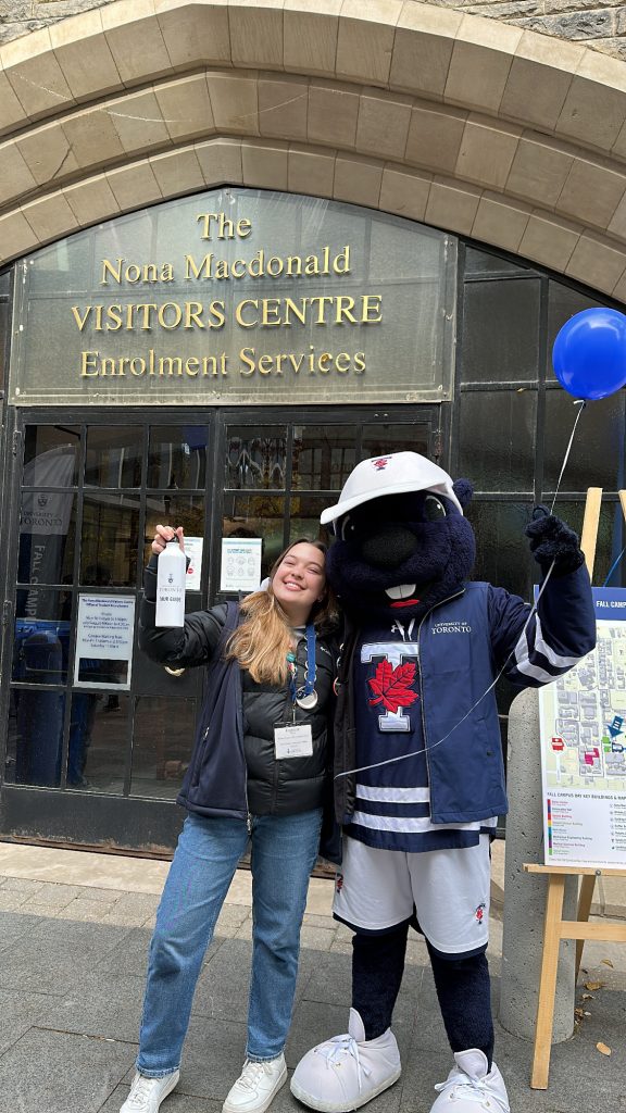 Photo of a student smiling standing next to a beaver mascot wearing a University of Toronto jersey