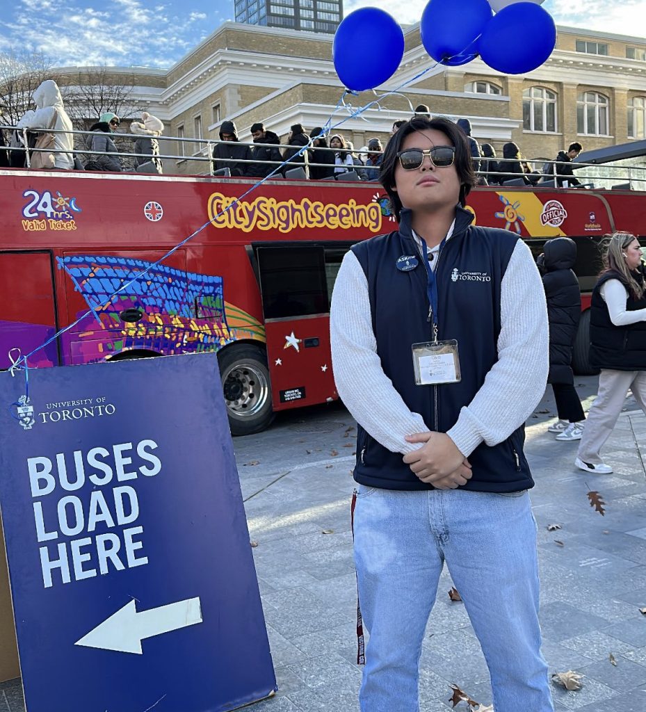 Photo of a student tour guide standing in front of a double-decker sightseeing bus