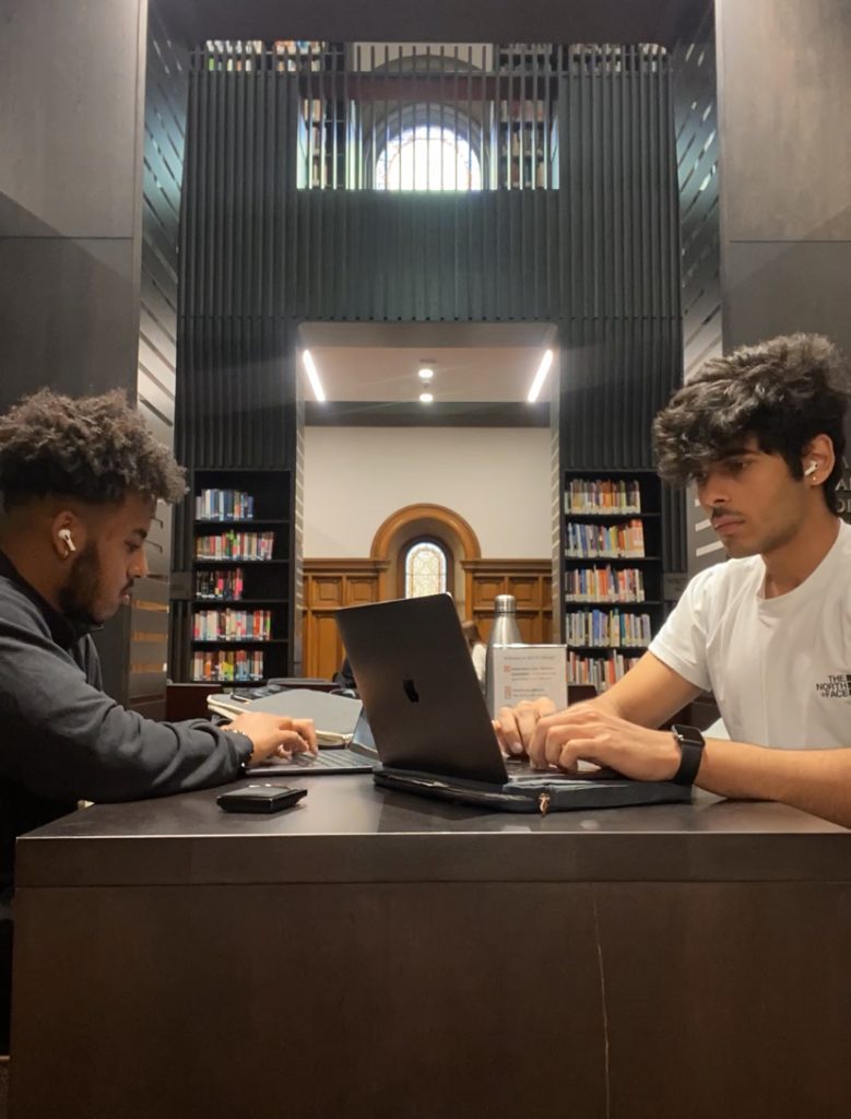Photo of 2 people studying on laptops in a library