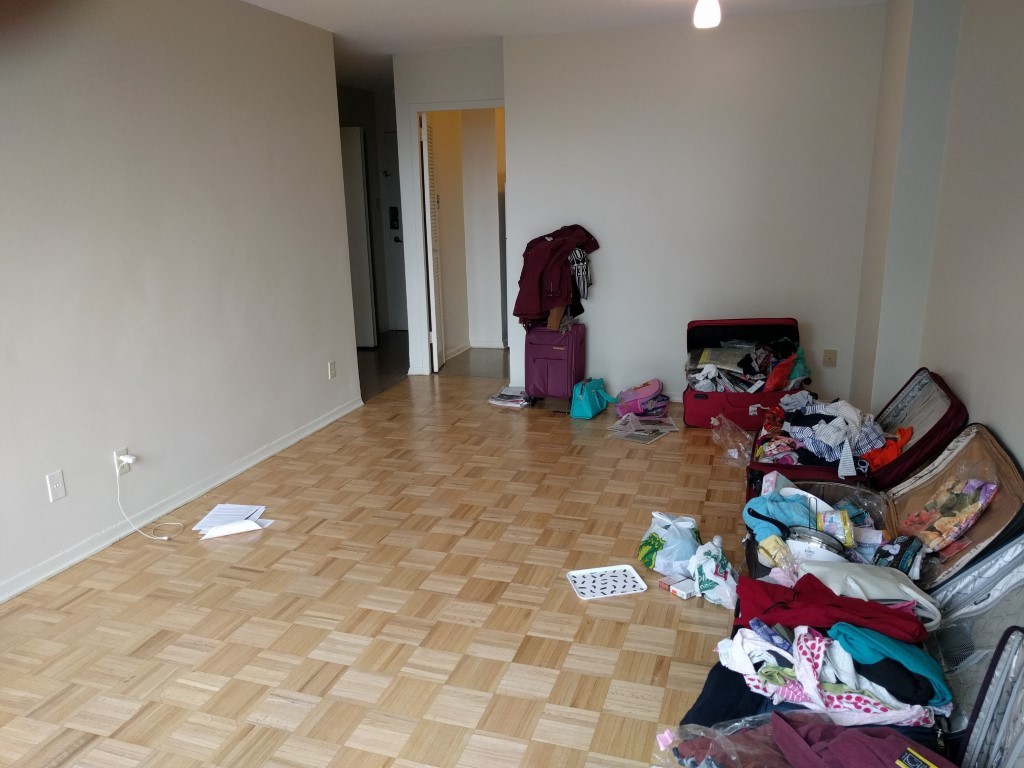 An interior of an apartment building with blank walls, a hardwood floor, and open suitcases along one side. Time to move in!  