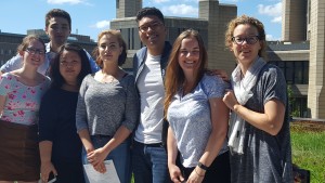 a team photo on the Rotman 4th floor balcony. Robarts library is shown in the background.