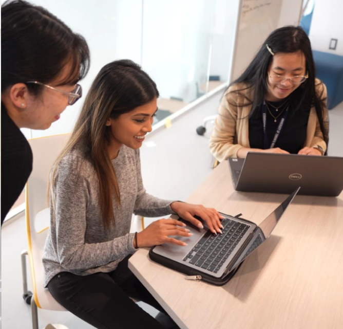 A project manager overseeing two students typing on their laptops.