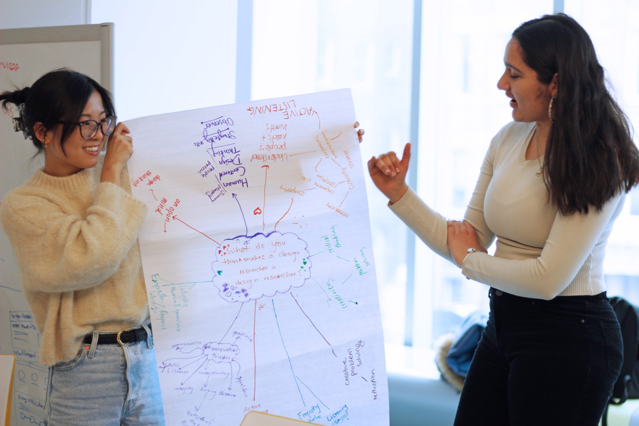 Person holding up chart paper with brainstorming on it and another person explaining what's on the chart