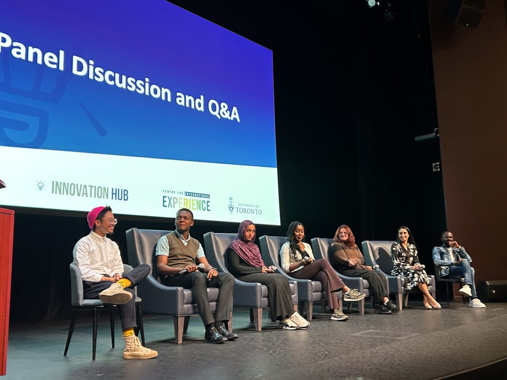 A photo of a Q&A panel session at the International Students: First 48 Hours In Canada" documentary screening, featuring seven participants seated on stage in discussion.