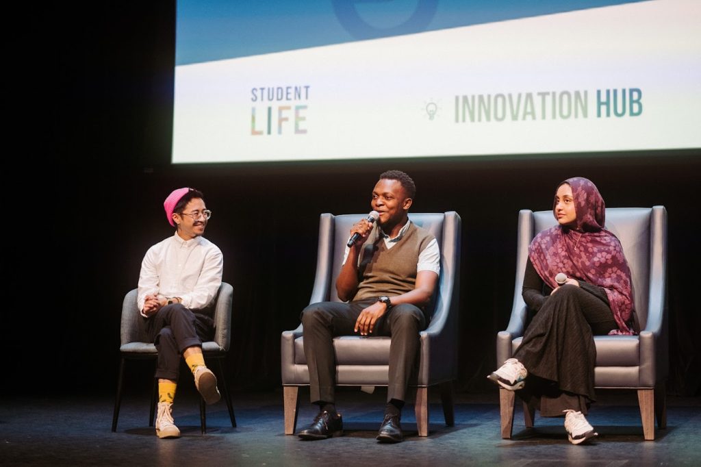 A photo of a Q&A panel discussion at the "International Students: First 48 Hours in Canada" documentary screening, featuring three panelists seated on stage, with one holding a microphone.