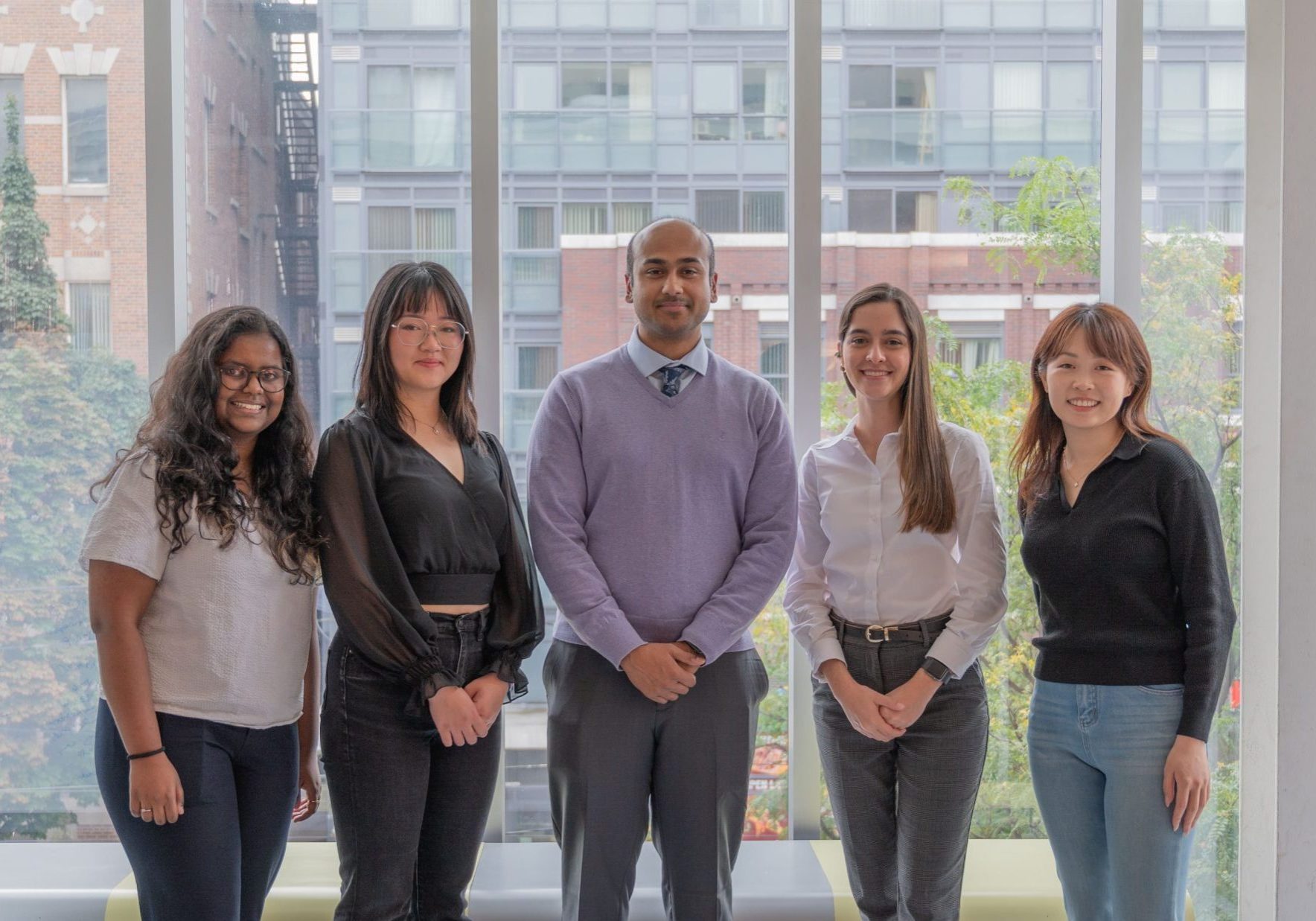 A photo of the "EDIA at School of the Environment" team, featuring five members standing indoors in front of large windows, smiling at the camera.