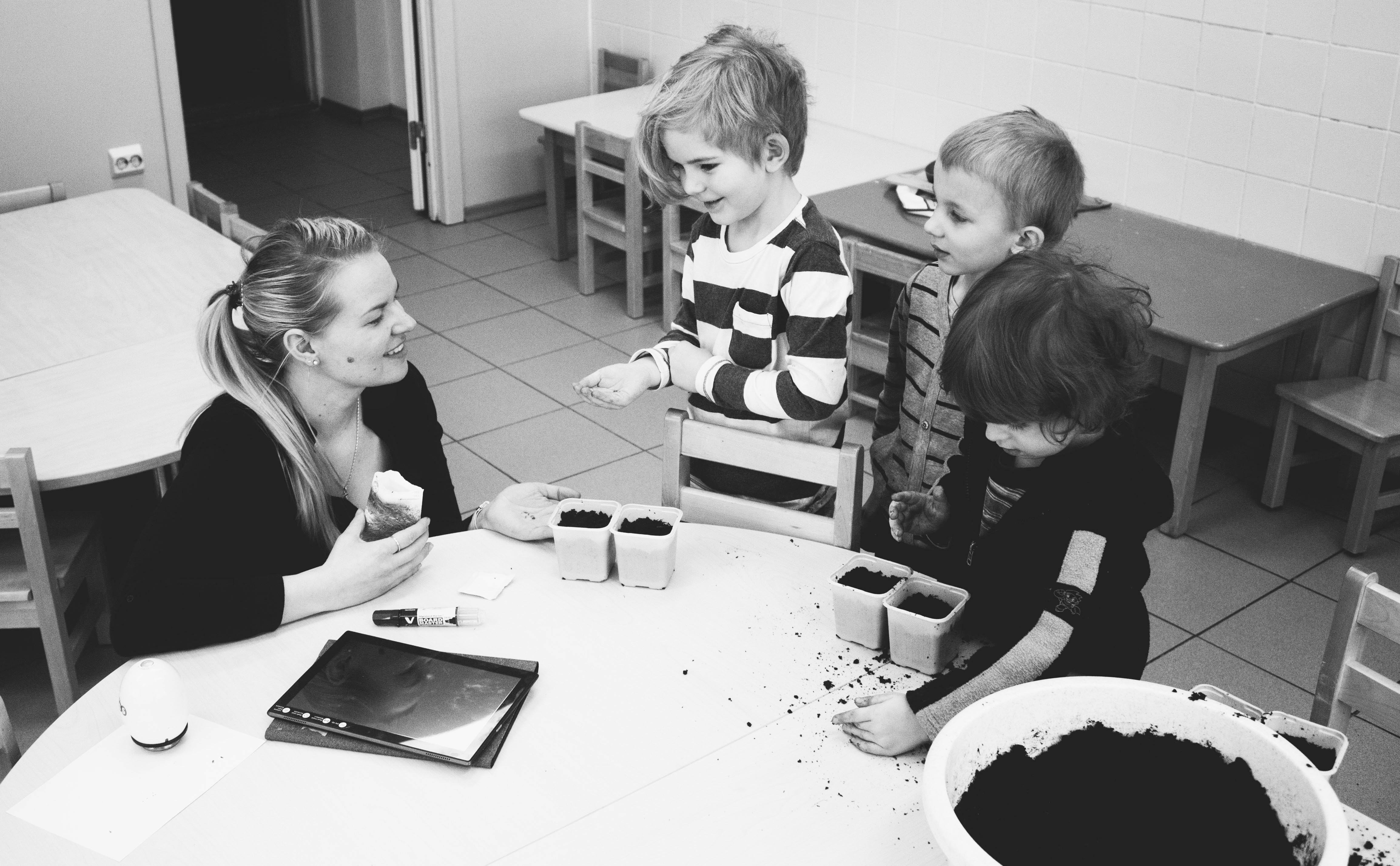 Teacher sitting with 3 young children at a table touching soil with their hands.