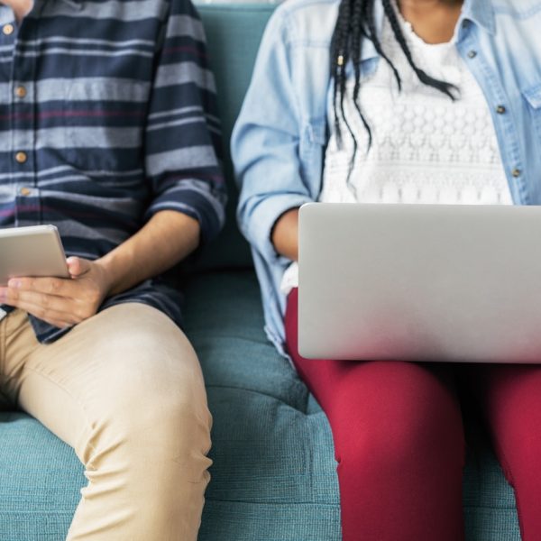 Two students sitting on a couch with laptops.