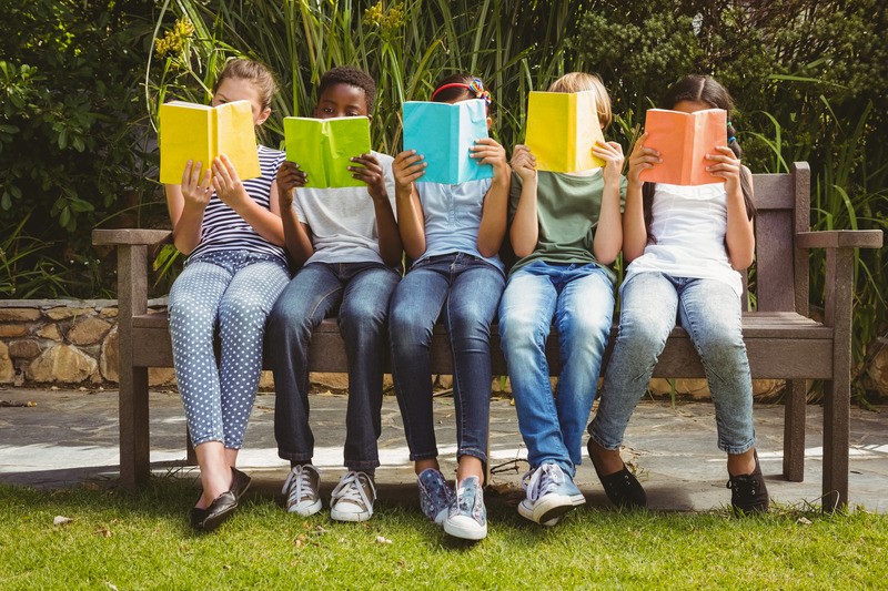Five children sitting on a bench reading colourful books.