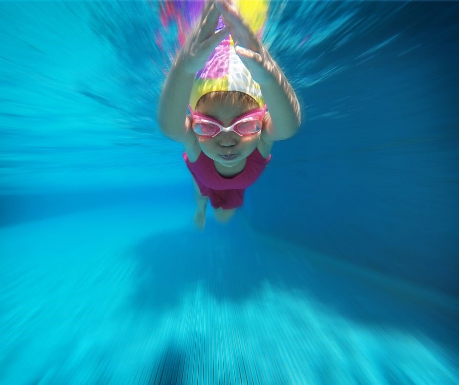 Child swimming in a pool wearing a pink swimsuit and goggles.