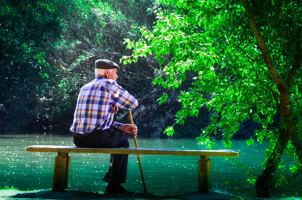 Senior sitting on a bench by the lake, while holding a cane