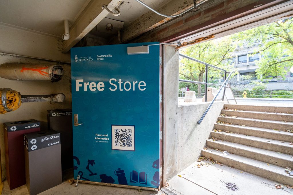 Image of the UTSG Free Store. Concrete stairs leading to the store with a big blue door that reads, "Free Store". Recycling bins on the side.