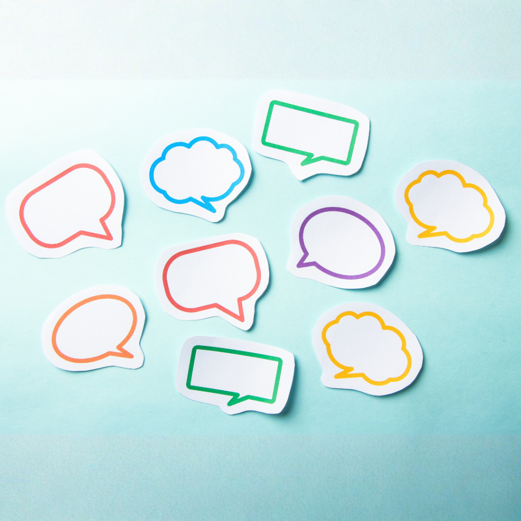  Assorted paper speech bubble cutouts with colorful outlines (red, blue, green, purple, yellow, and orange) scattered on a light blue background, symbolizing conversation or communication.