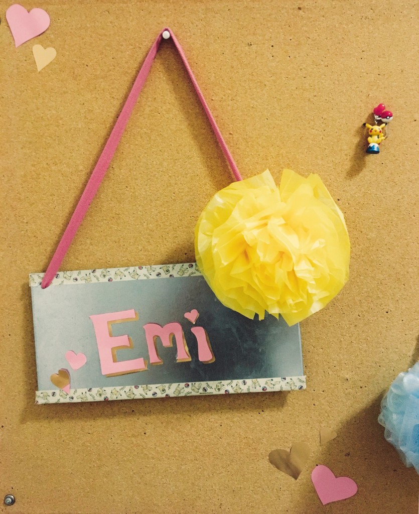 A picture of Emi's dorm bulletin board, with a sign that says "Emi" and a paper flower.
