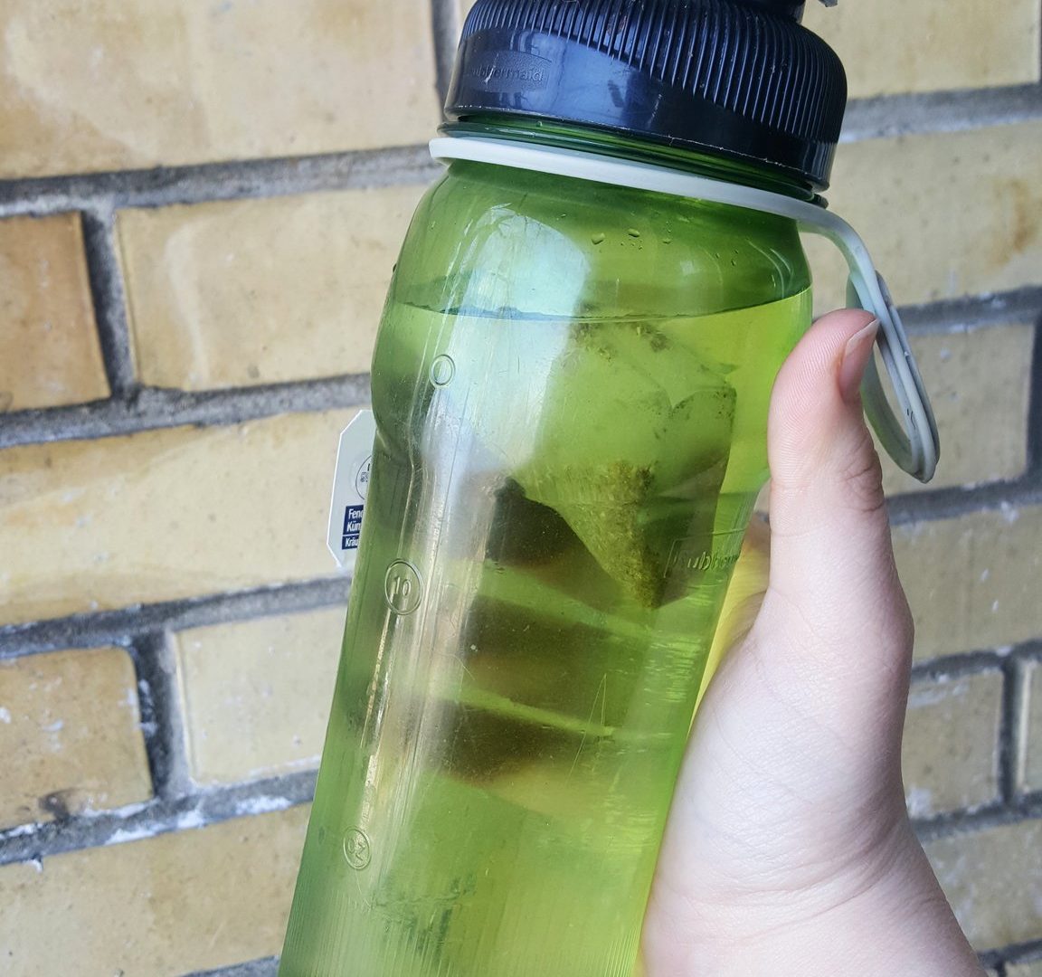a hand gripping a green reusable water bottle with a tea bag inside of it
