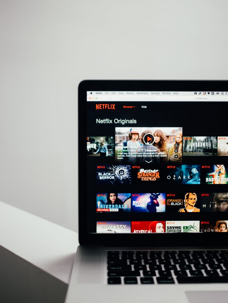 A macbook screen shows a range of Netflix show titles.
