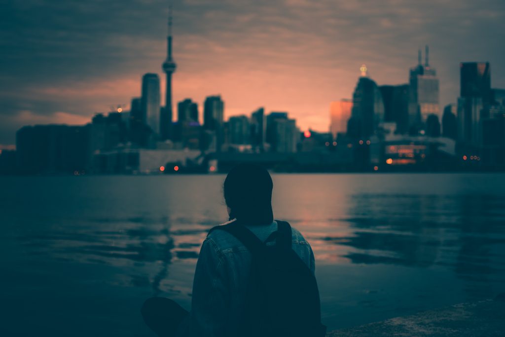 As night falls, a person stands and looks at the Toronto skyline.