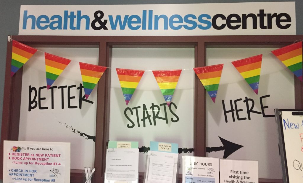 A sign that says: "health & wellness centre: better starts here" with rainbow pride flags