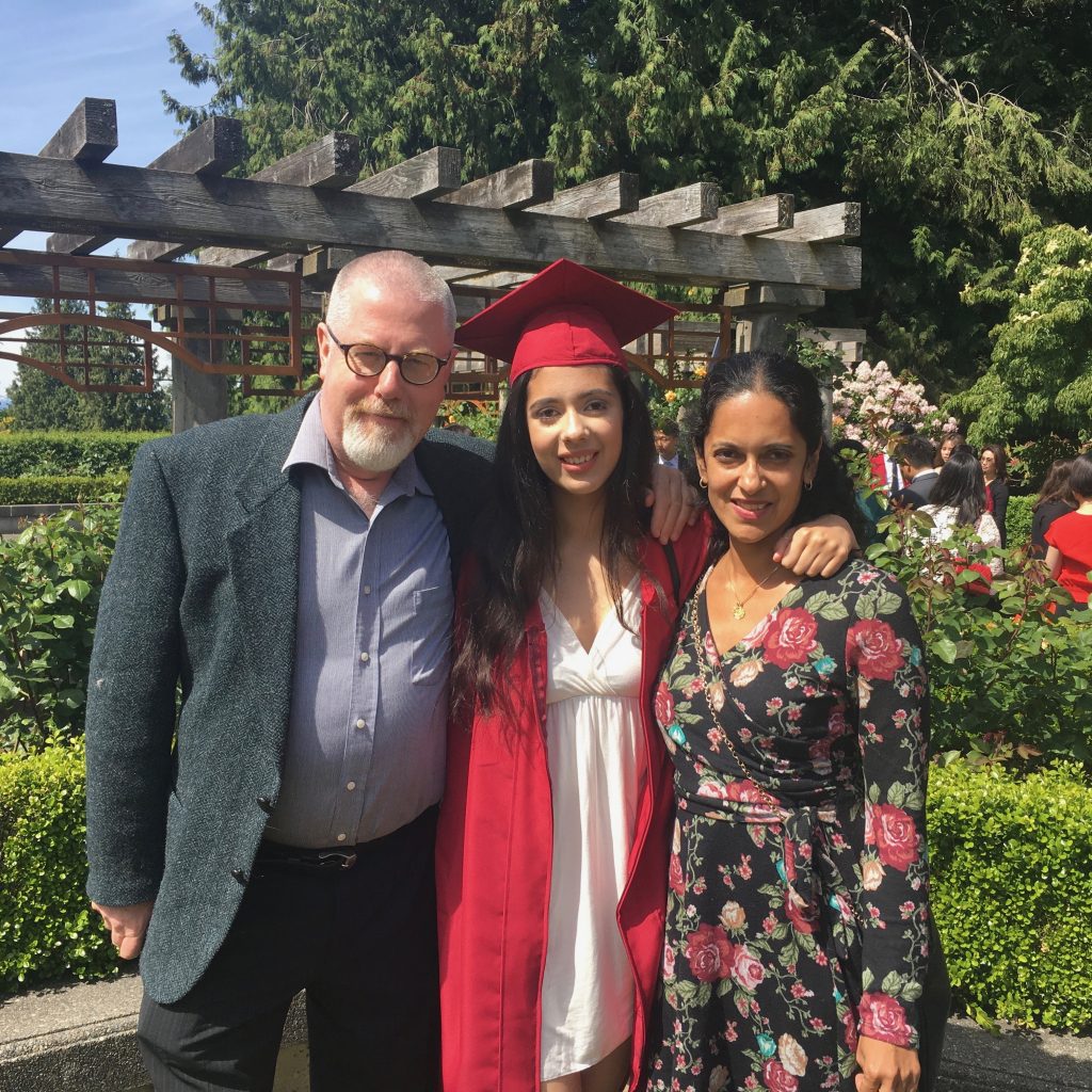 Student blogger Talia stands with her parents wearing a graduation robe and cap