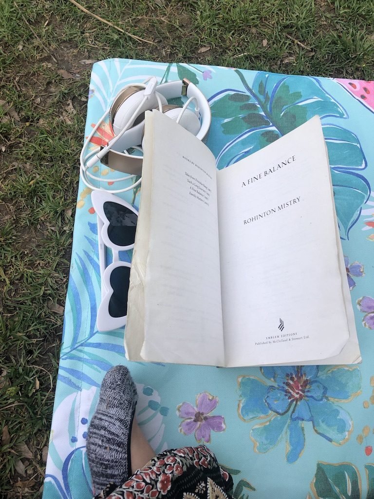 A book, a pair of sunglasses and headphones on a towel on the grass.