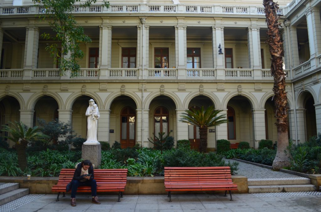 a woman is seated on a bench, texting, in one of the quads of the Catholic University in Santiago