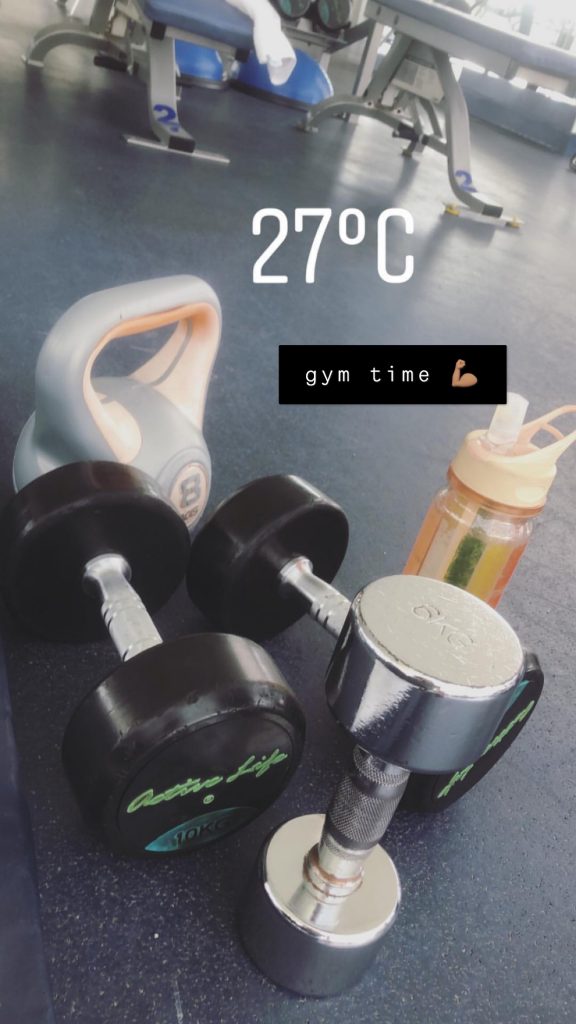 A couple of dumbells and a water bottle set on the floor. There's a water stamp that reads 27 degrees celcius. There's also text with a black background that reads "gym time".