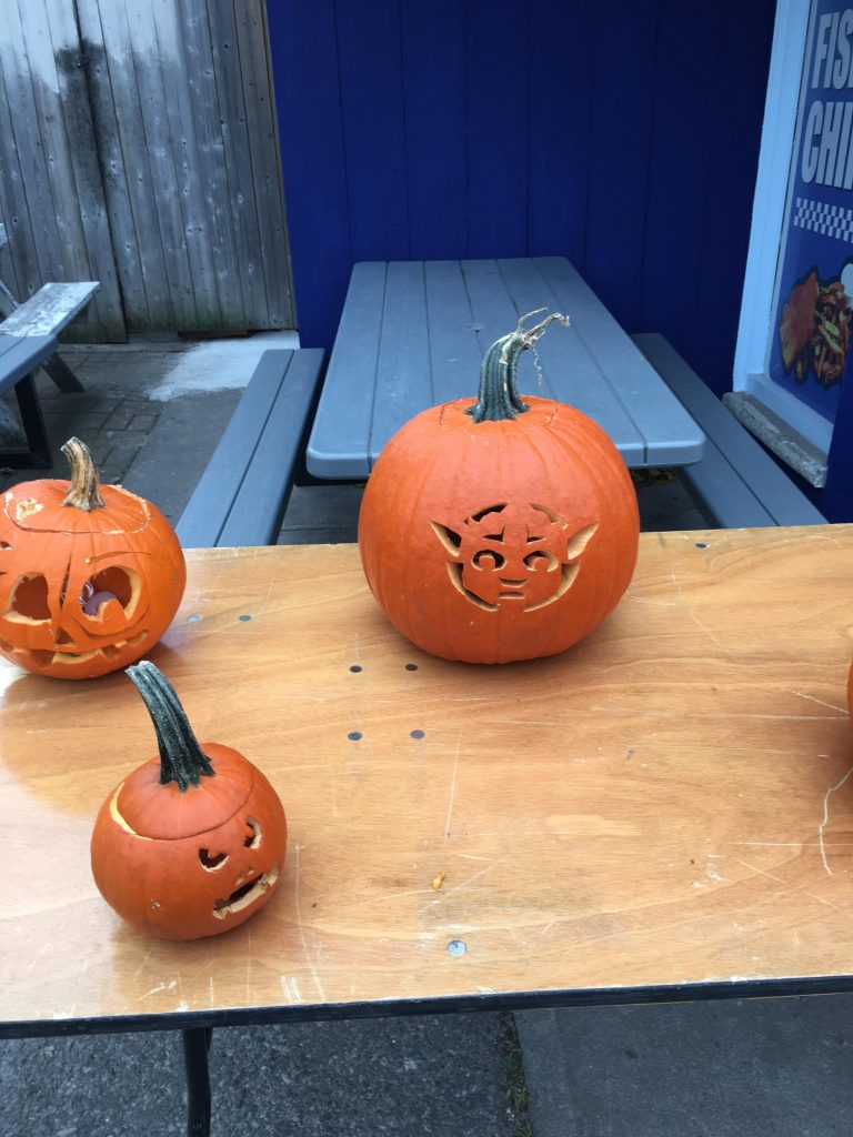 Three carved pumpkins on a table, and one is Yoda.