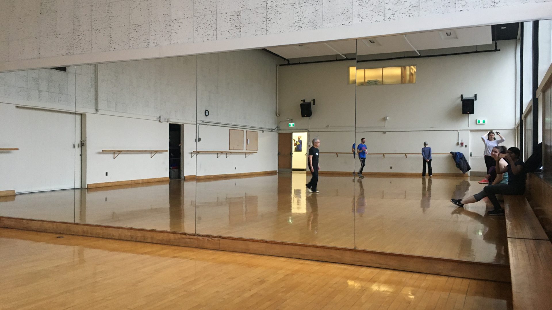 A large mirror fills an entire wall, which reflects a wood panelled room. A few people are milling around.