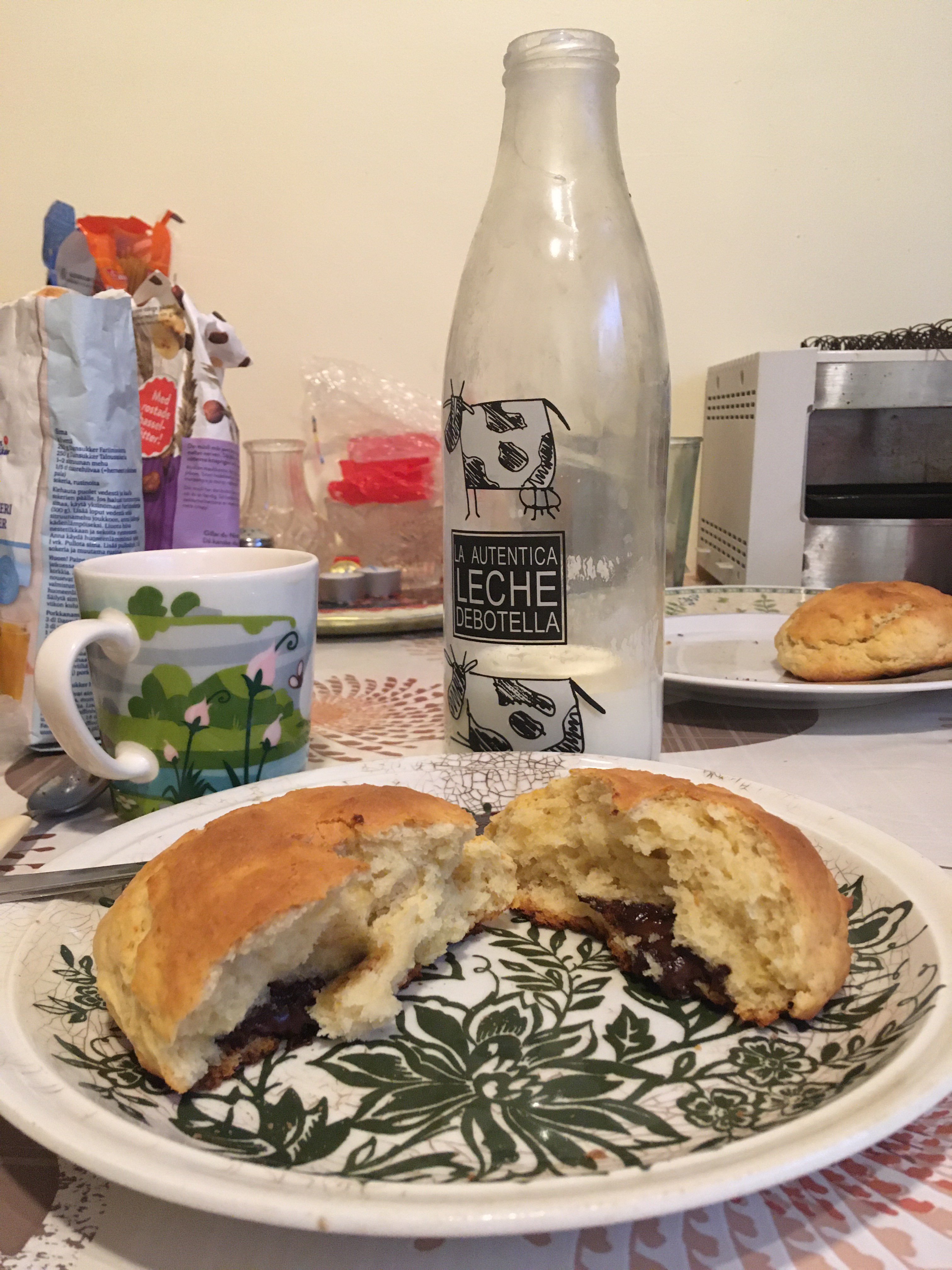 A scone sits broken in half on a plate, in front of a glass bottle of milk
