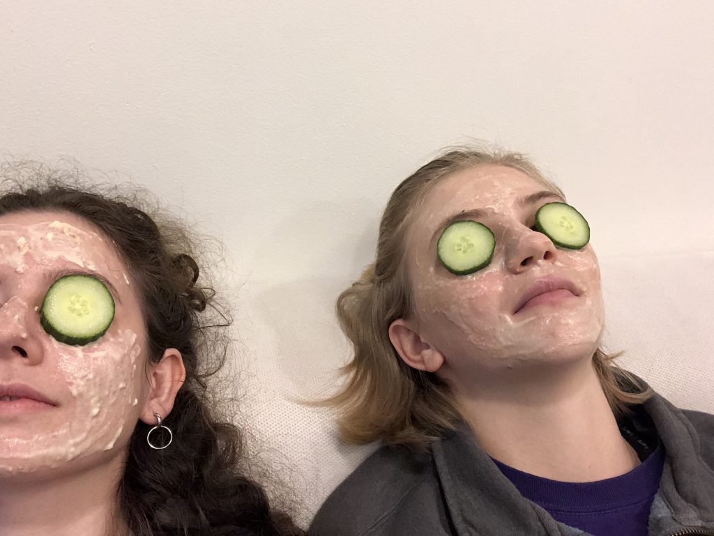 Friend and I wearing face masks with cucumber over our eyes.