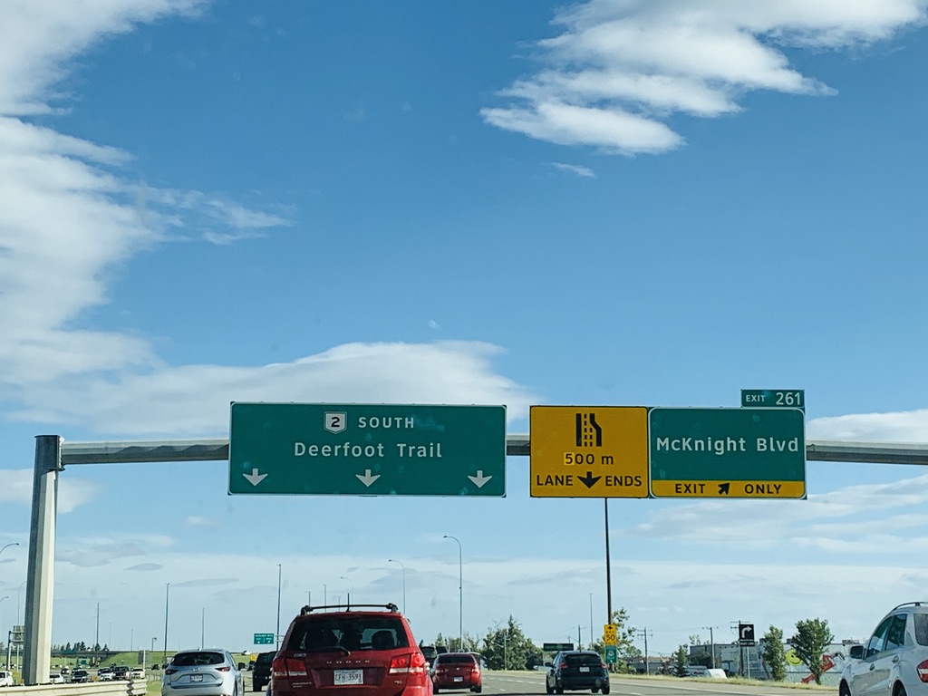 red vehicle and other multicolored vehicles on a highway, below a traffic sign that reads "Deerfoot Trail"