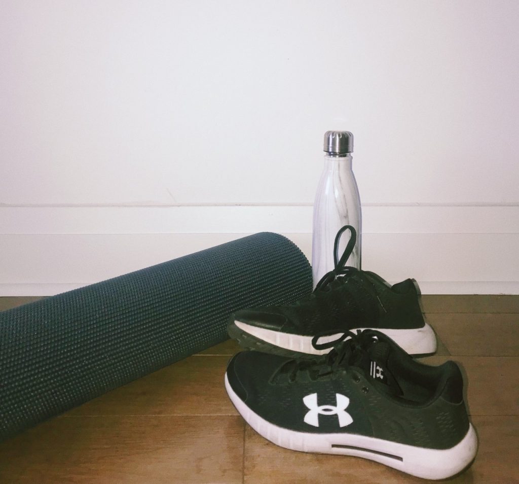 image of a pair of black and white running shoes, a white water bottle and a black yoga mat