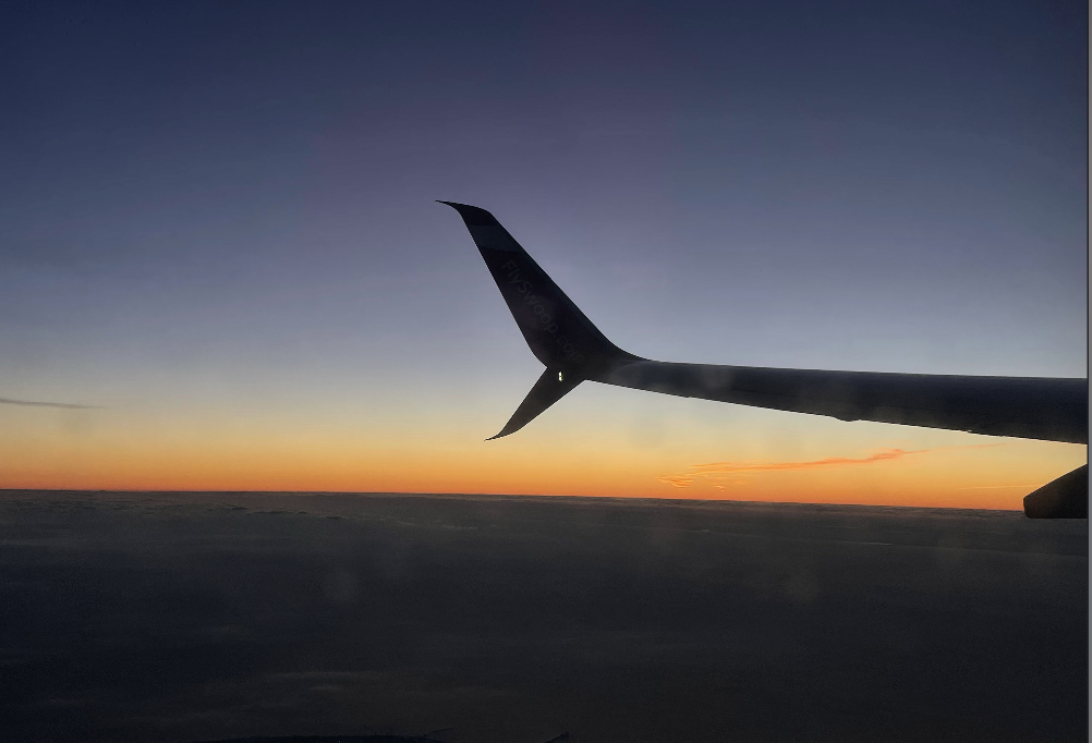 picture of a sunrise from the inside of the plane, with the wing in the view