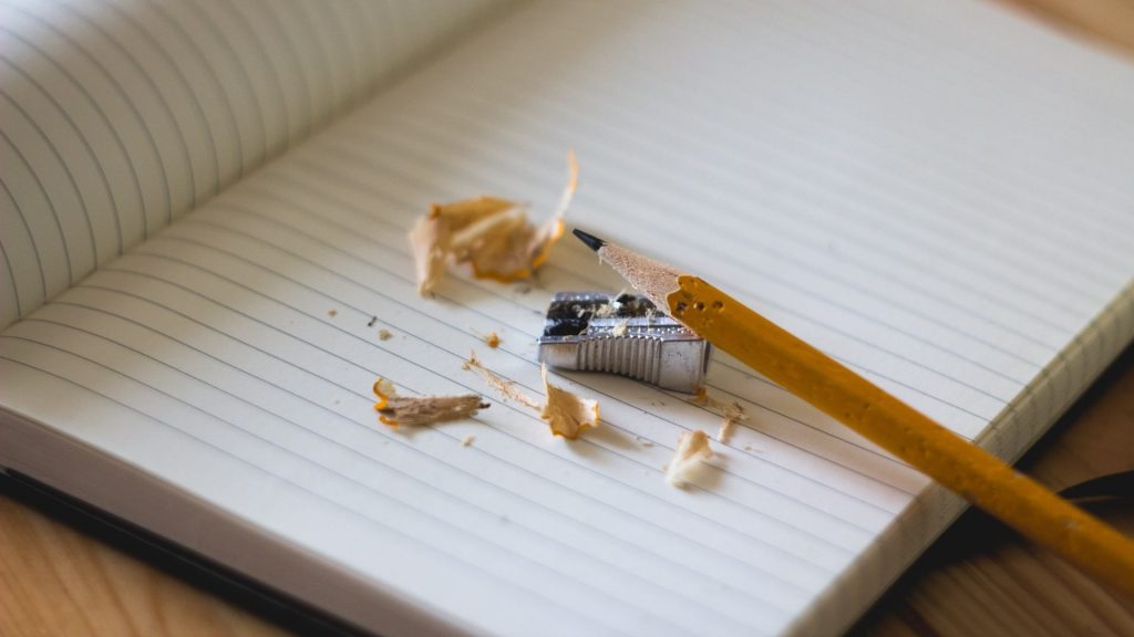 A freshly sharpened pencil perched on a sharpener and empty lined notebook.