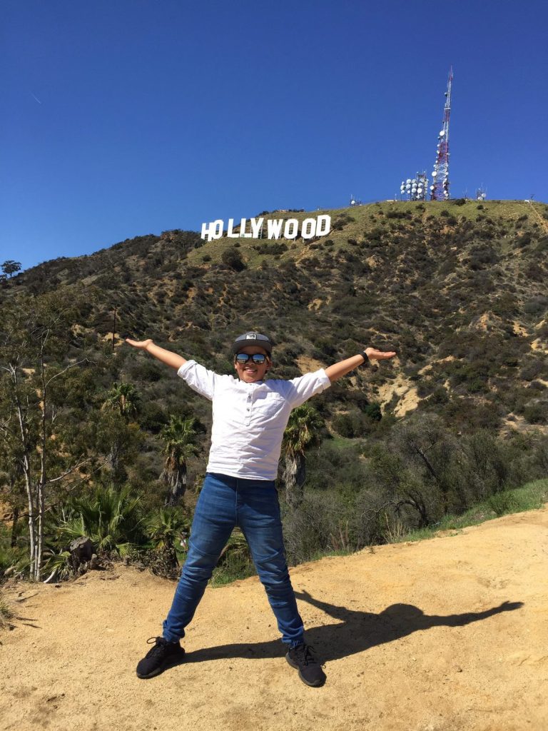 Photo of a person with their arms outstretched in front of the Hollywood sign