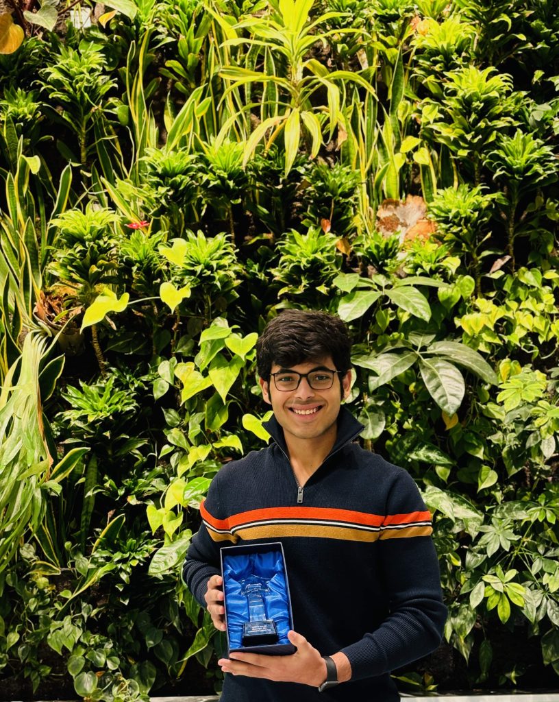 Photo of Yashvit holding a trophy in front of a plant wall