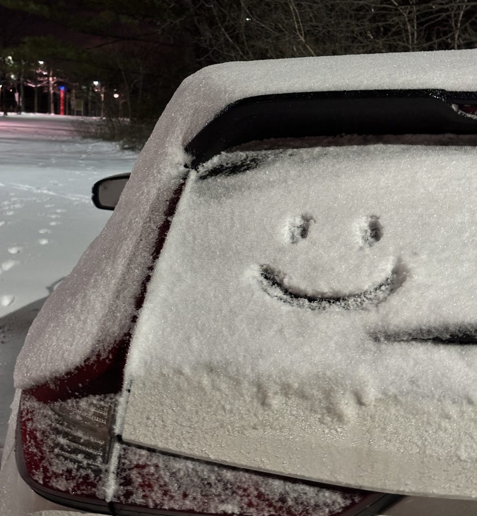 Car covered with snow with a smiley face carved out.