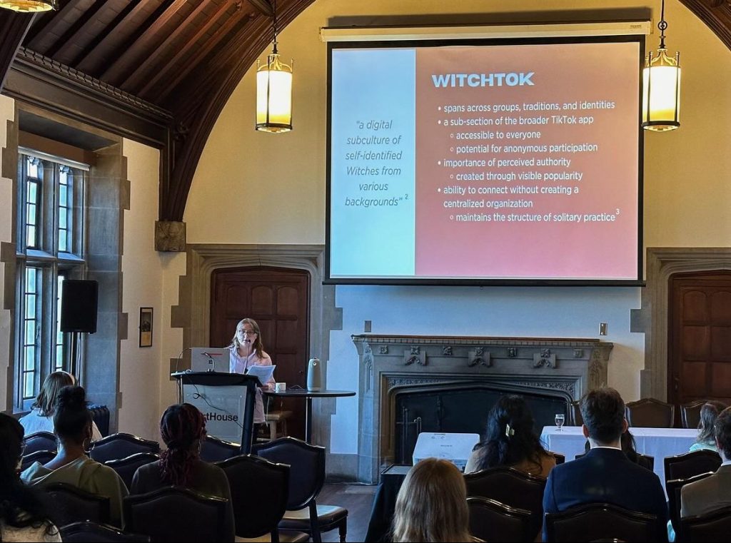 Woman presenting at a podium in front of a screen with a presentation slide titled "WITCHTOK"